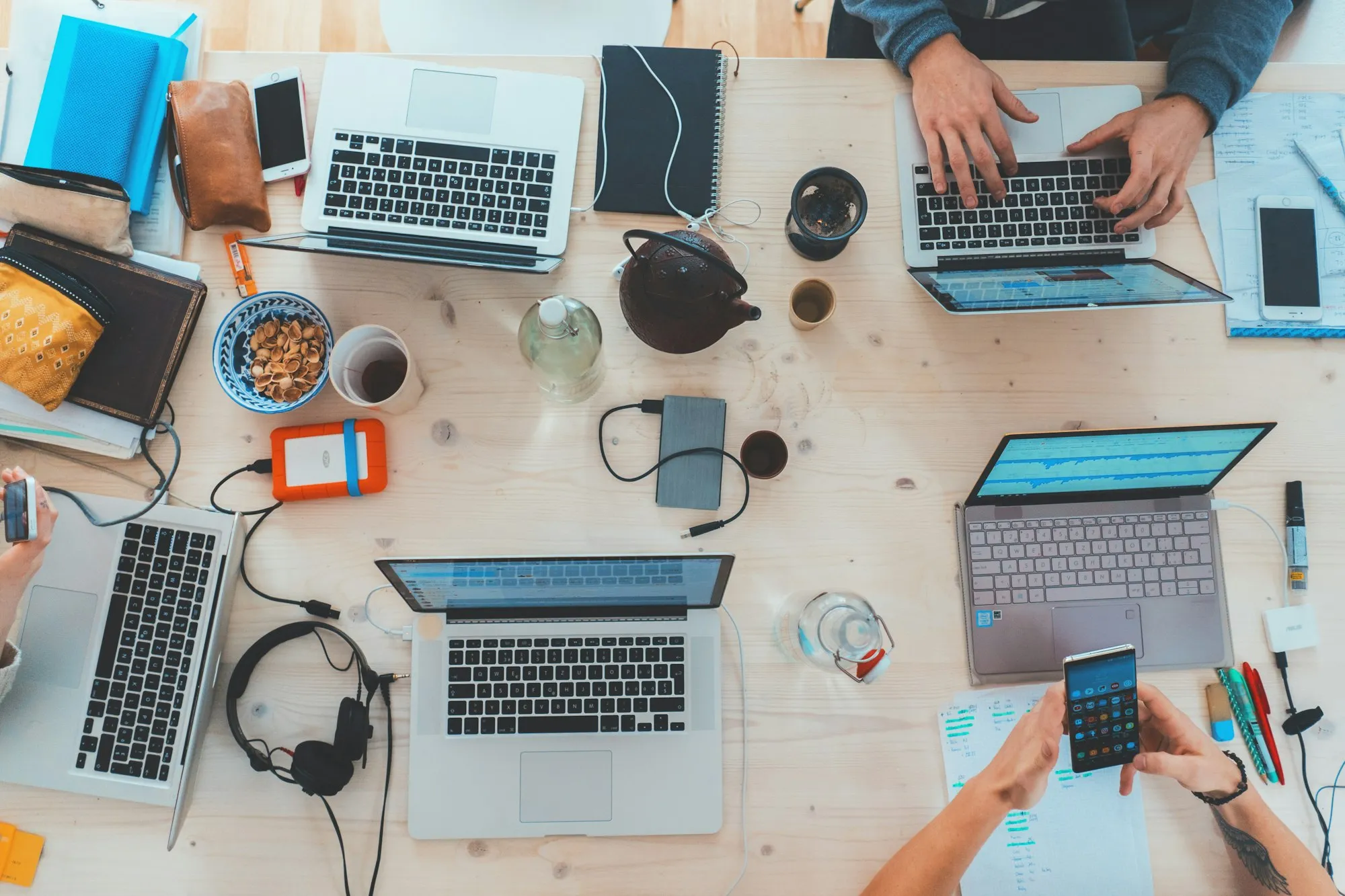 A shared desk with several laptops, notes and devices in use at once